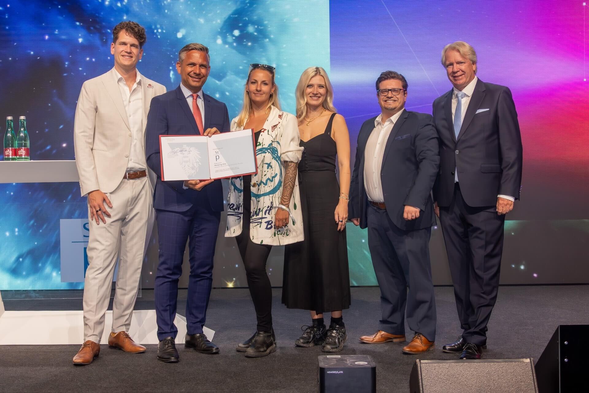 Das Marketingkonzept „Hidden talents: Wenn Vorurteile Karrieren machen“ von OBI Bau- und Heimwerkermärkte holte beim Staatspreis Marketing 2026 den ersten Platz in der Sonderpreis-Kategorie Internal Marketing und Employer Branding: Wirtschaftsminister Wolfgang Hattmannsdorfer und Willy Lehmann, Präsident Austrian Marketing Confederation, gratulieren dem Marketingteam um Melli Schomann (Leitung Marketing), Alexander Eisner (Brand and Campaign Manager International), Jessica Lechner (Marketing & Communication Manager) und Dominik Hackl (Creative Core)